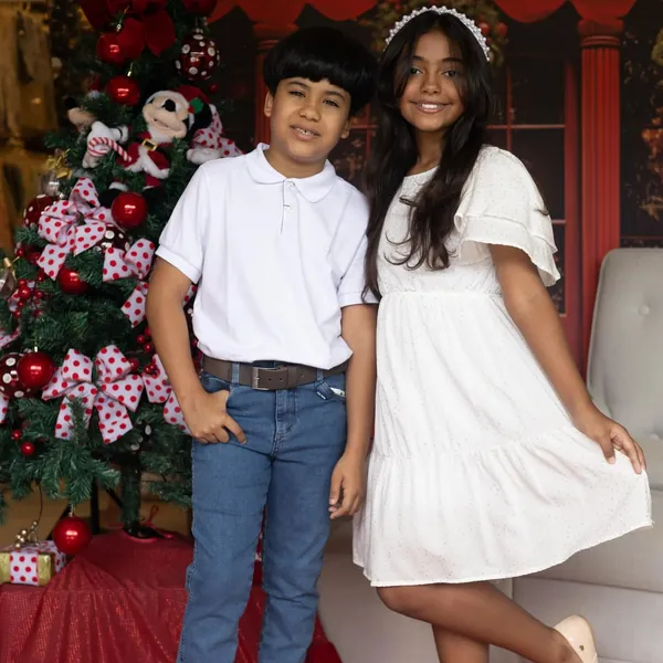 Menino e menina com looks brancos de festa ao lado da árvore de Natal